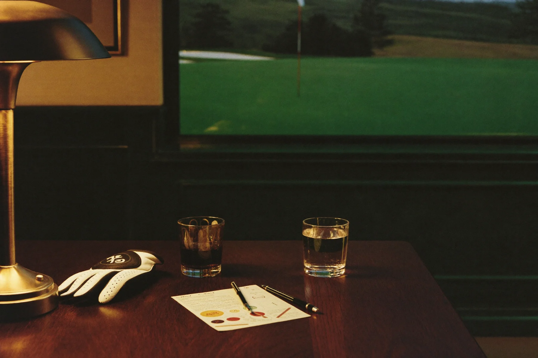Scorecards and drinks on a wooden Clubhouse table overlooking a putting green