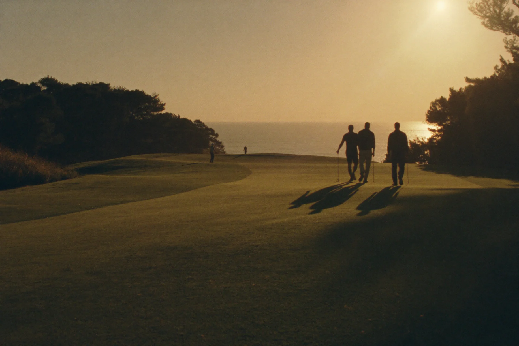 Golfers walking towards the sea in the last light of an evening round