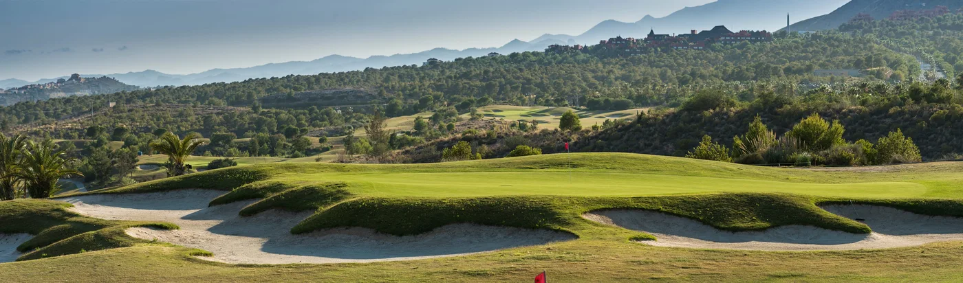 Poniente Course green and bunkers beneath wooded hills