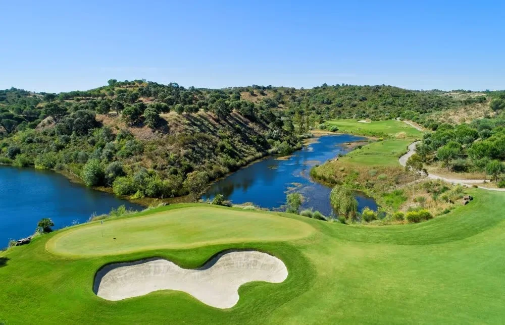 Elevated view of a Monte Rei green and bunker beside a winding lake