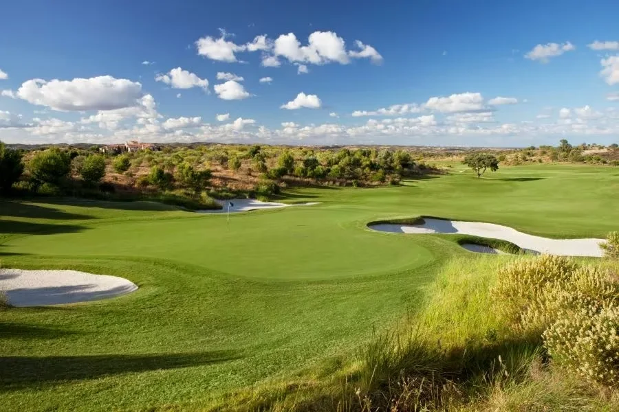 Monte Rei North Course green with white sand bunkers under a blue sky